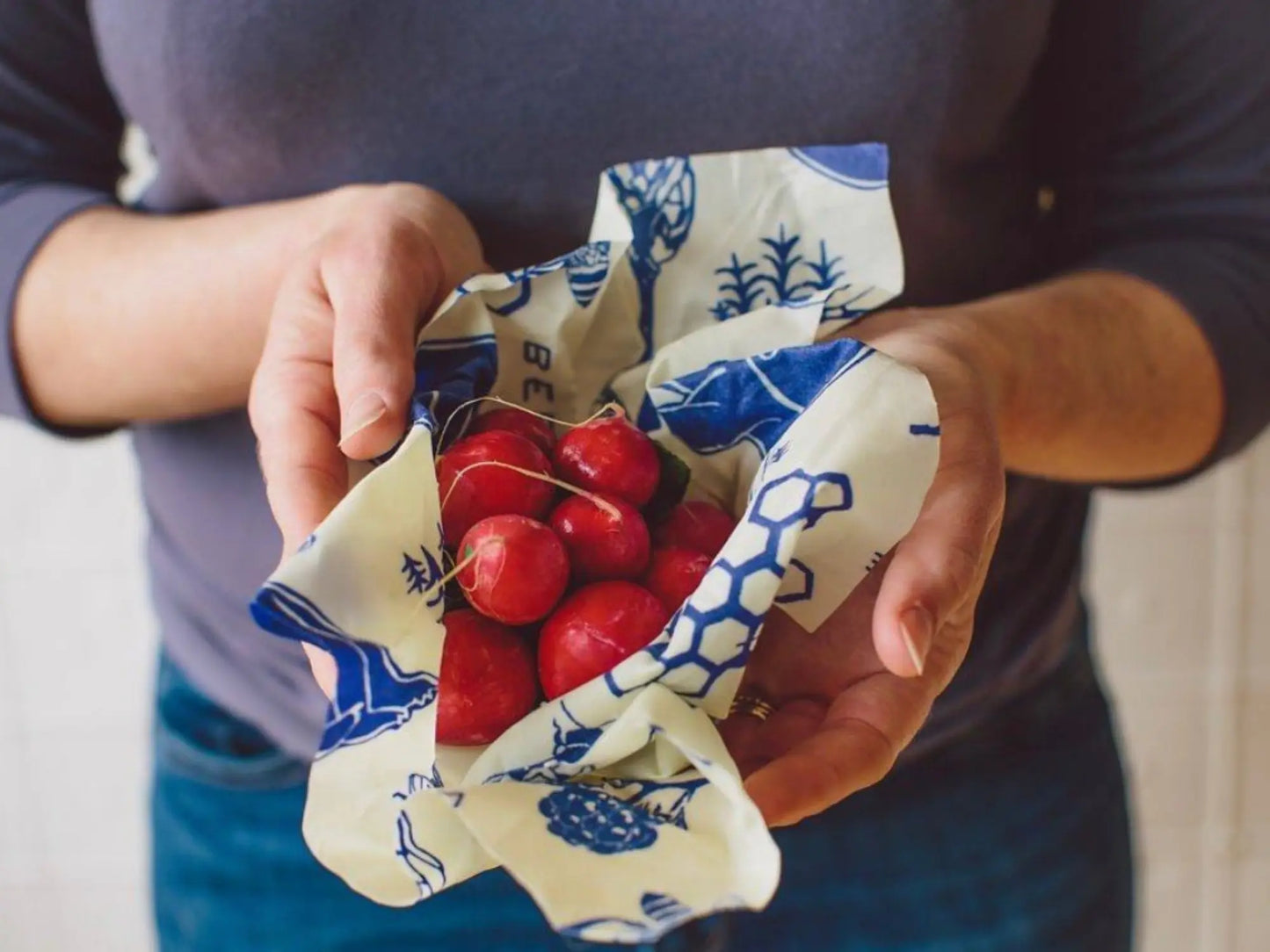Person holding a small bag of radishes wrapped in reusable food wrap with blue pattern