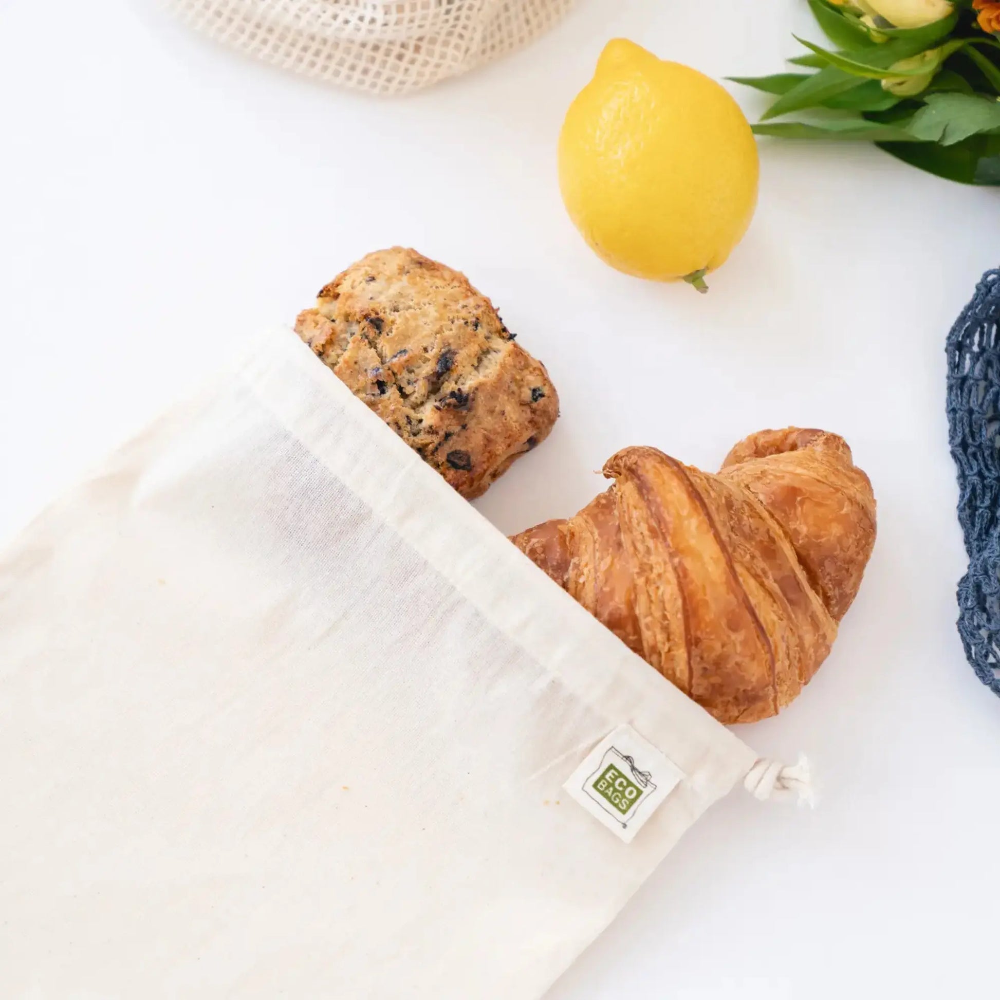 Reusable eco bag with croissant, lemon, and flowers on a white surface