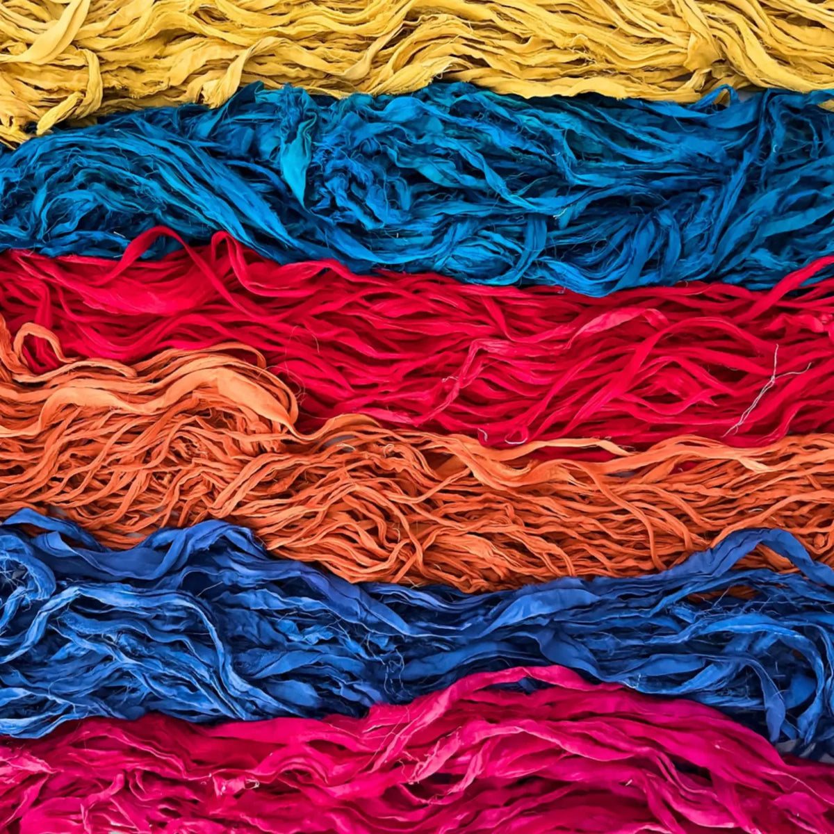 Close-up of recycled sari silk chiffon ribbon in bands of gold, teal, red, orange, blue, and pink, showing the soft, ruffled texture