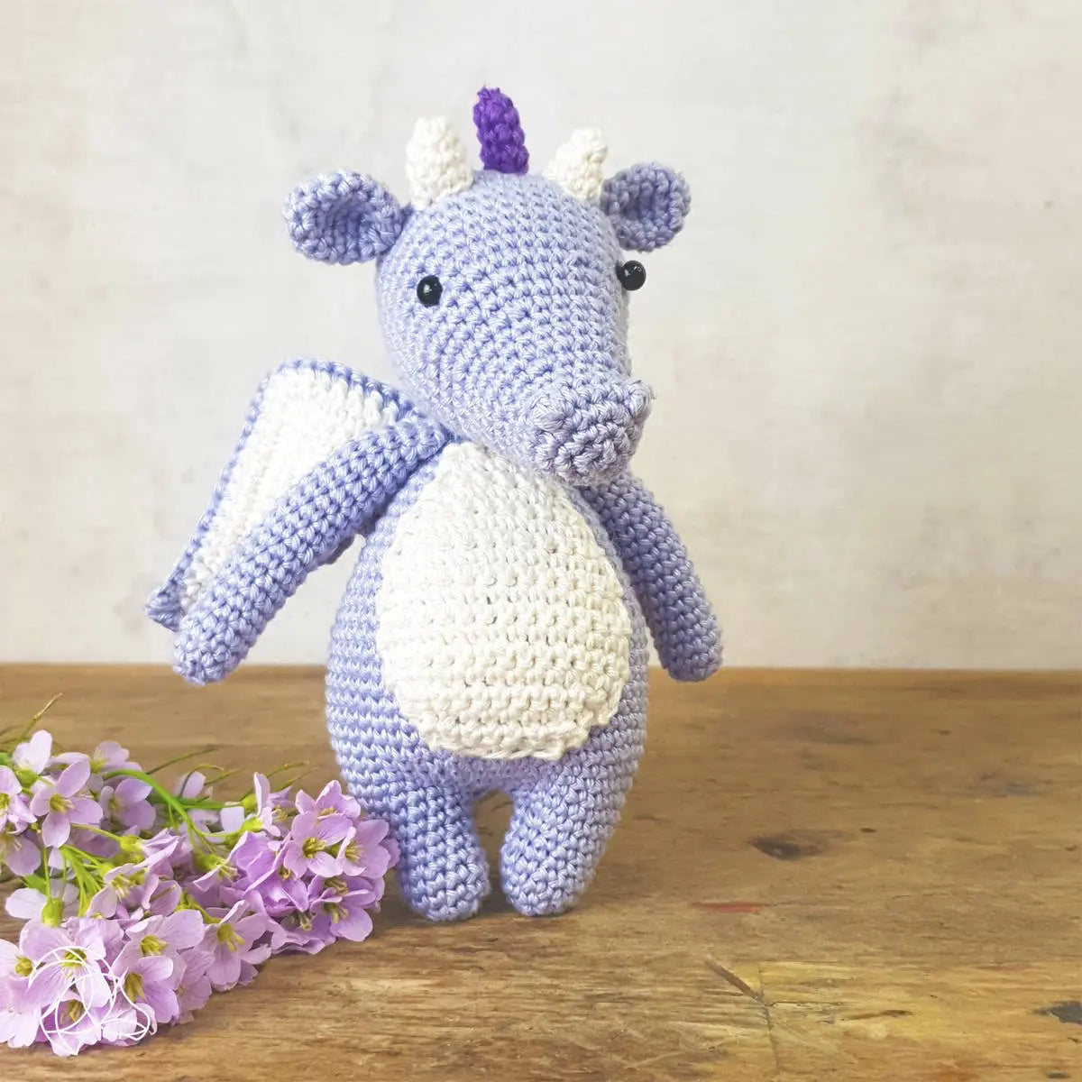 Lilac handmade crochet dragon lifestyle with flowers on wooden surface