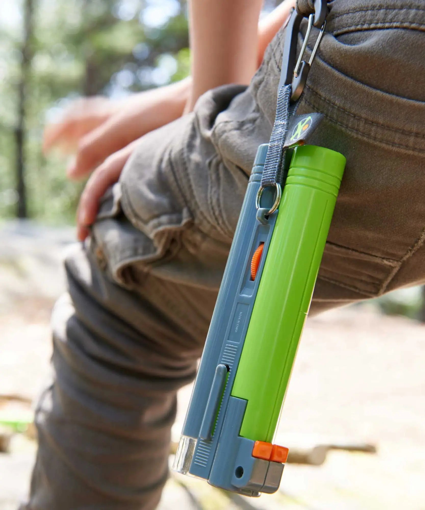 Green and blue tool attached to a person's pants with a blurred natural background