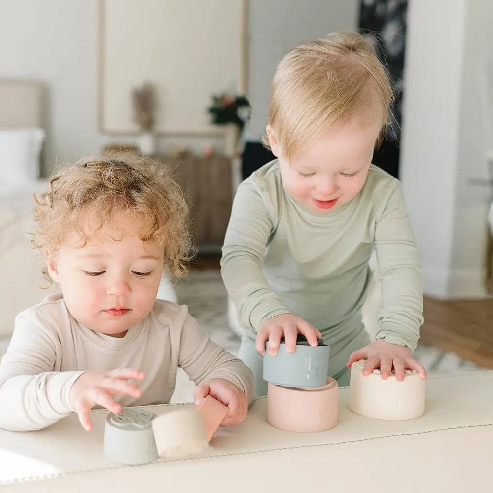 Two young toddlers playing with stacking toys on a light-colored surface.