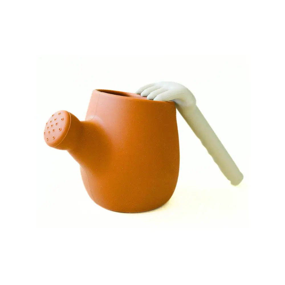 Terracotta-colored children's watering can with a white handle on a white background