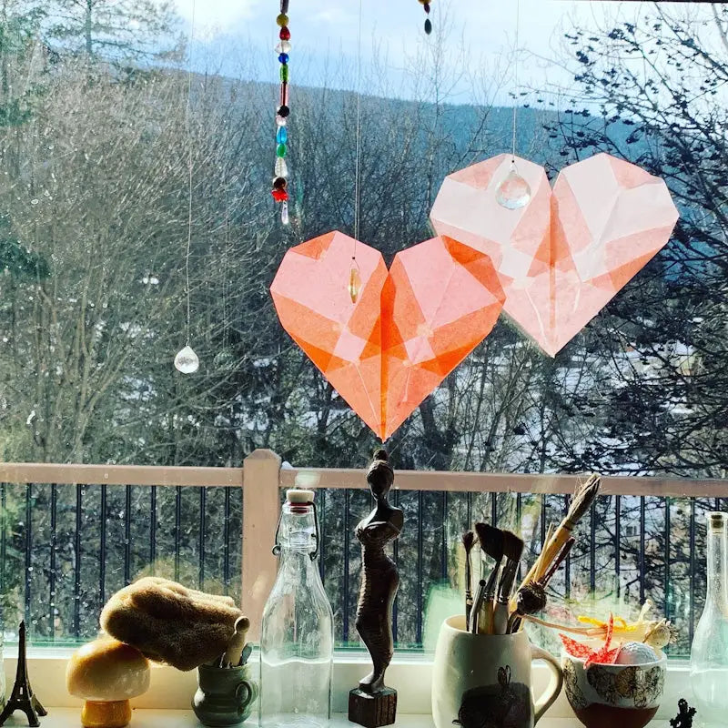two pink hearts hanging in front of a window made from Japanese silk paper