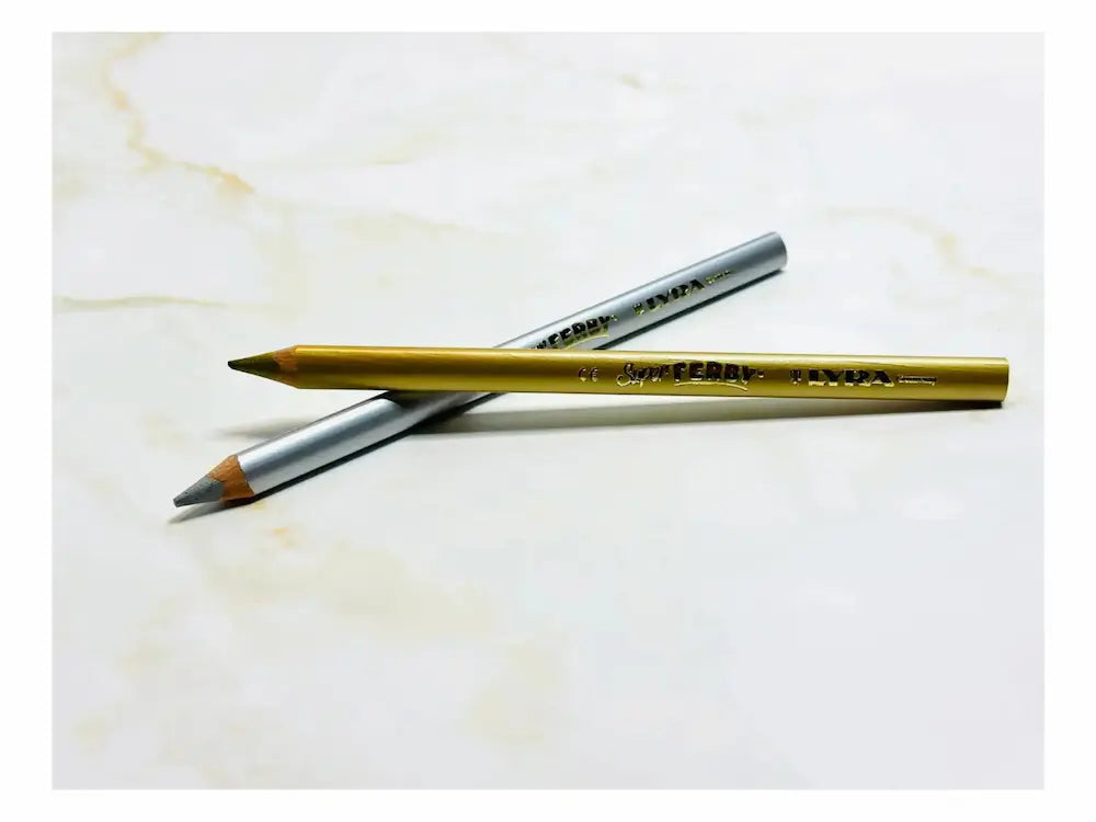 Two pencils, one gold and one silver, on a marble surface