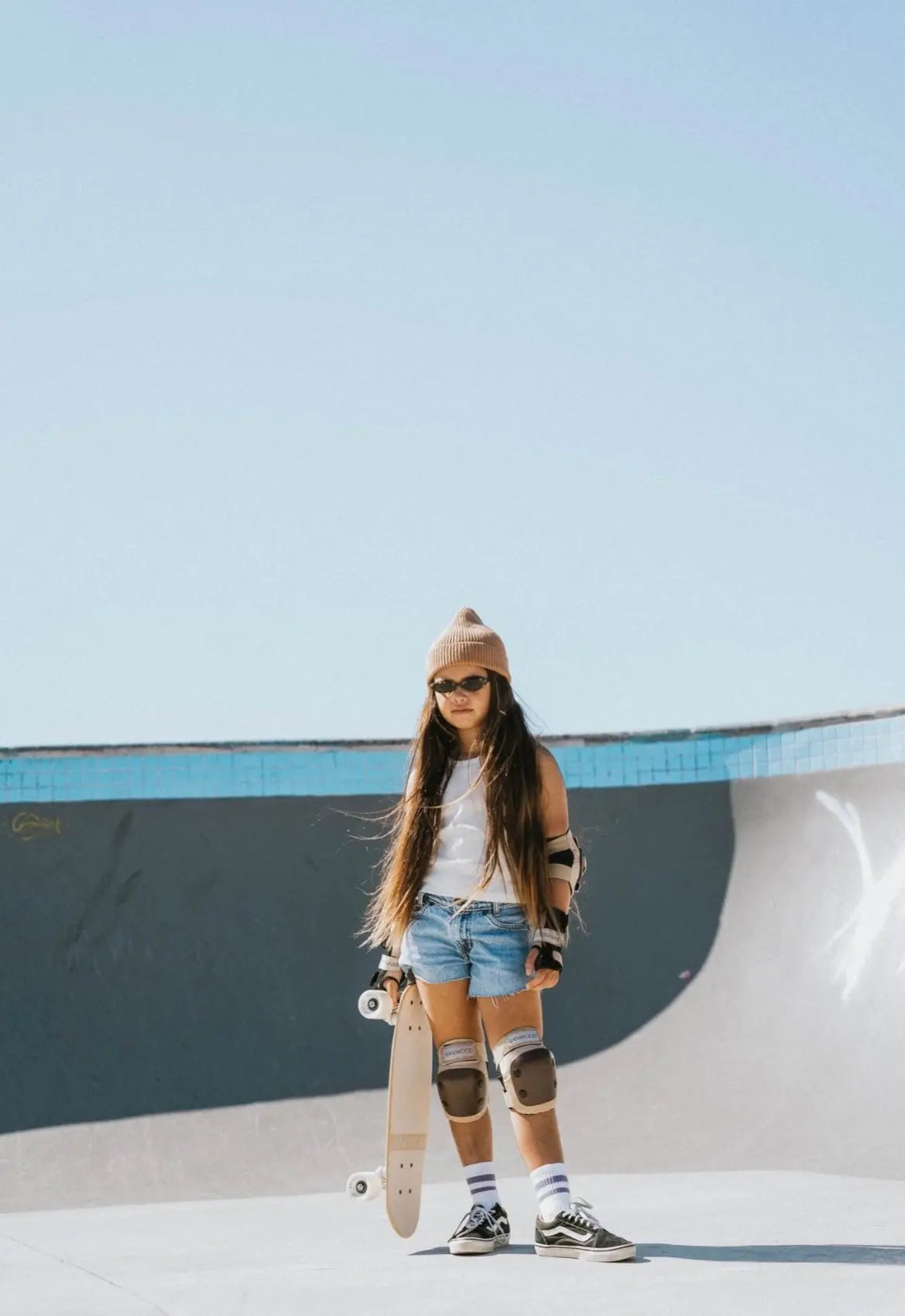 Kid with a skateboard at a skate park with a clear blue sky.