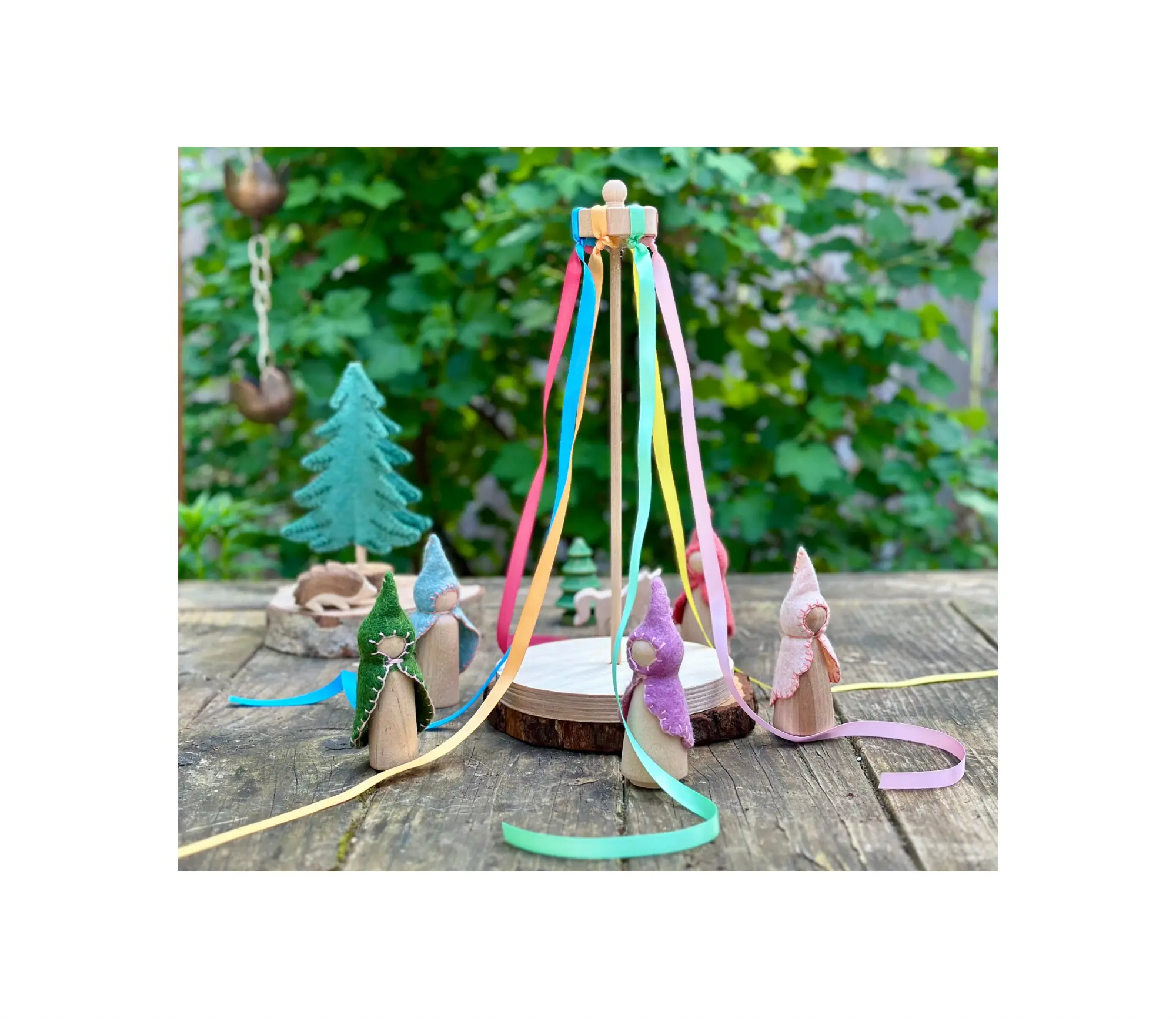 Wooden fairies with colorful ribbons on a wooden surface with a green leafy background.