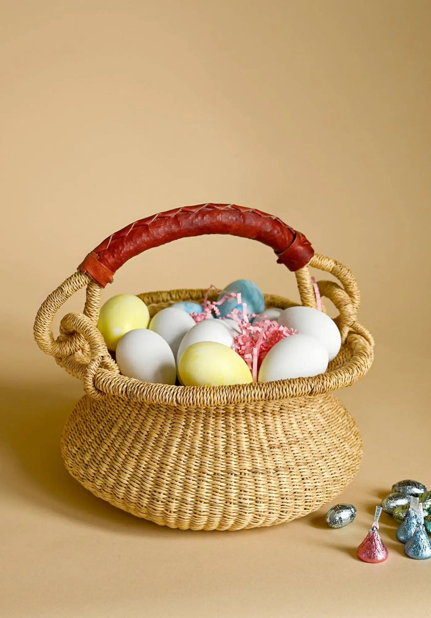 Wicker baby bolga basket with Easter eggs and small toys on a beige background