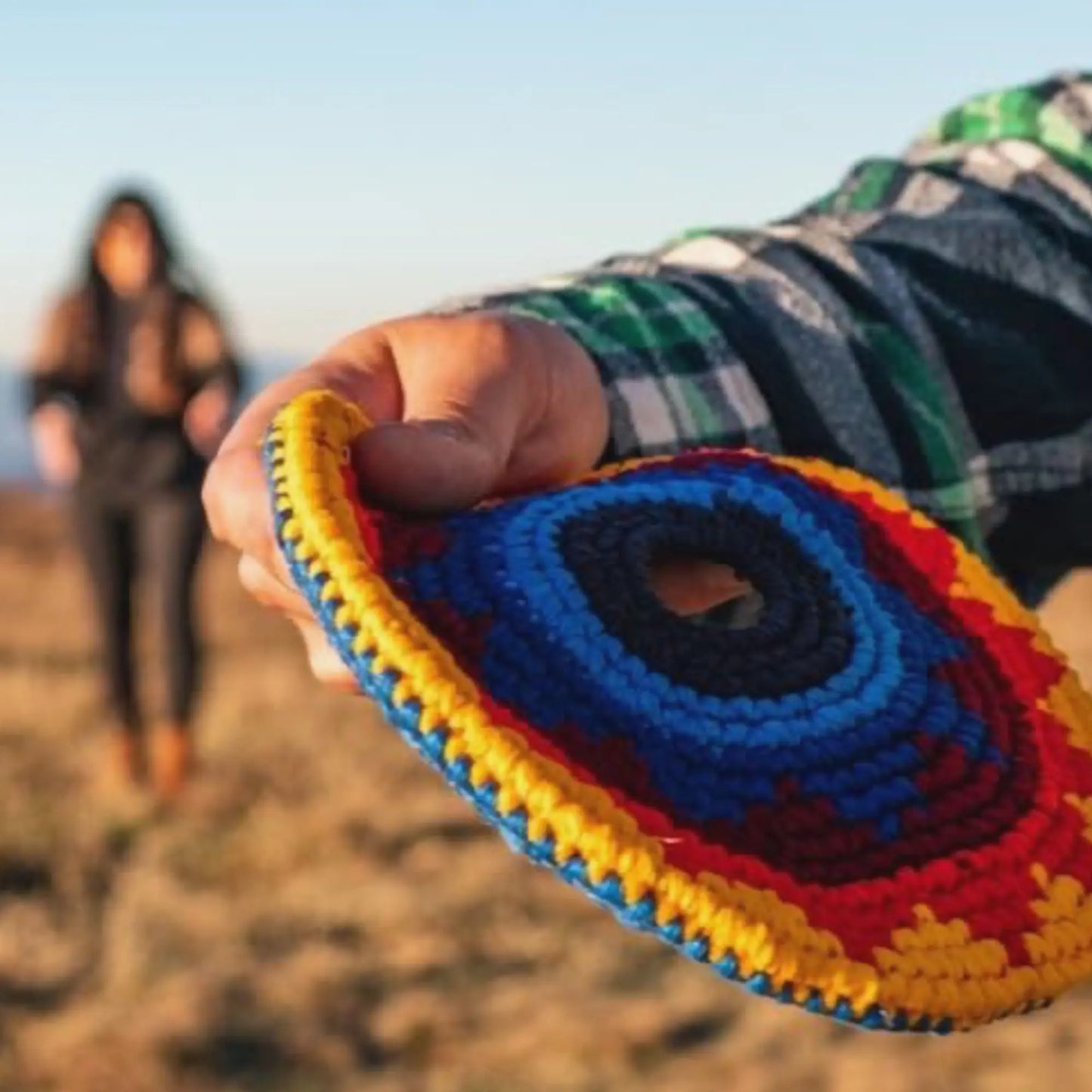 Colorful indoor outdoor soft frisbee held by a person with a blurred background of a person walking on a path.