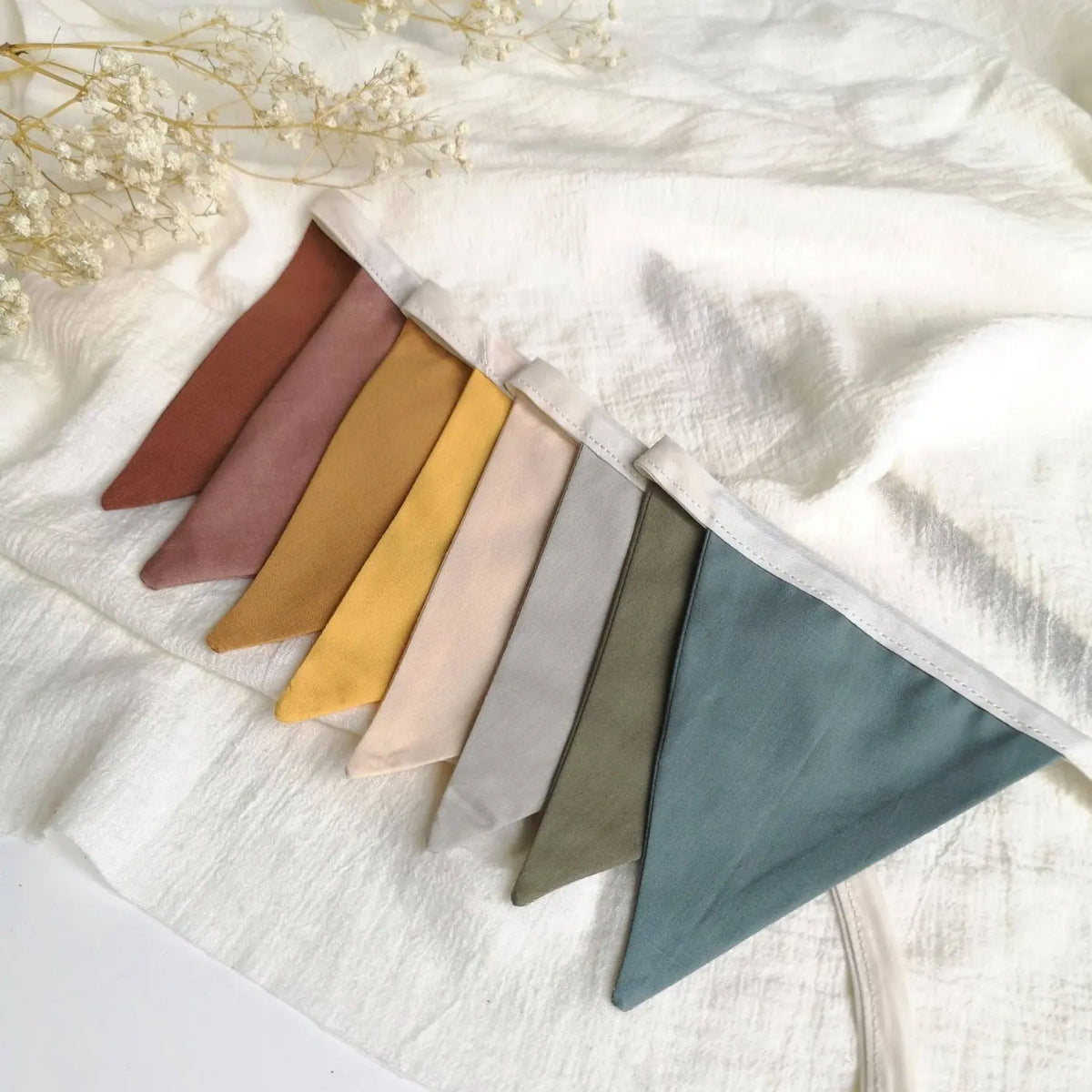 Soft rainbow linen pennant garland laid flat to show the full muted color palette of warm and cool earthy tones.
