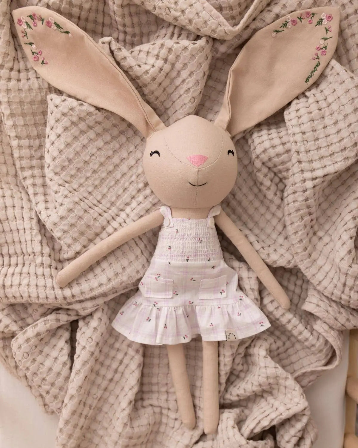 Doll with floral dress and embroidered bunny ears on a textured fabric background