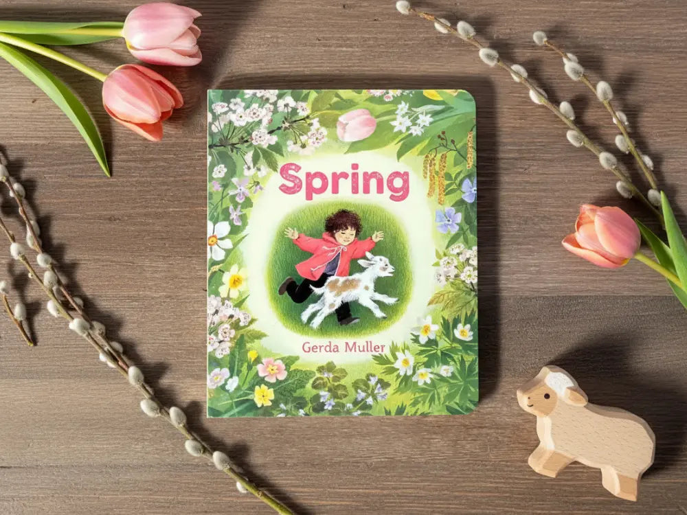 Book titled 'Spring' by Gerda Muller on a wooden surface with flowers and a toy cow.