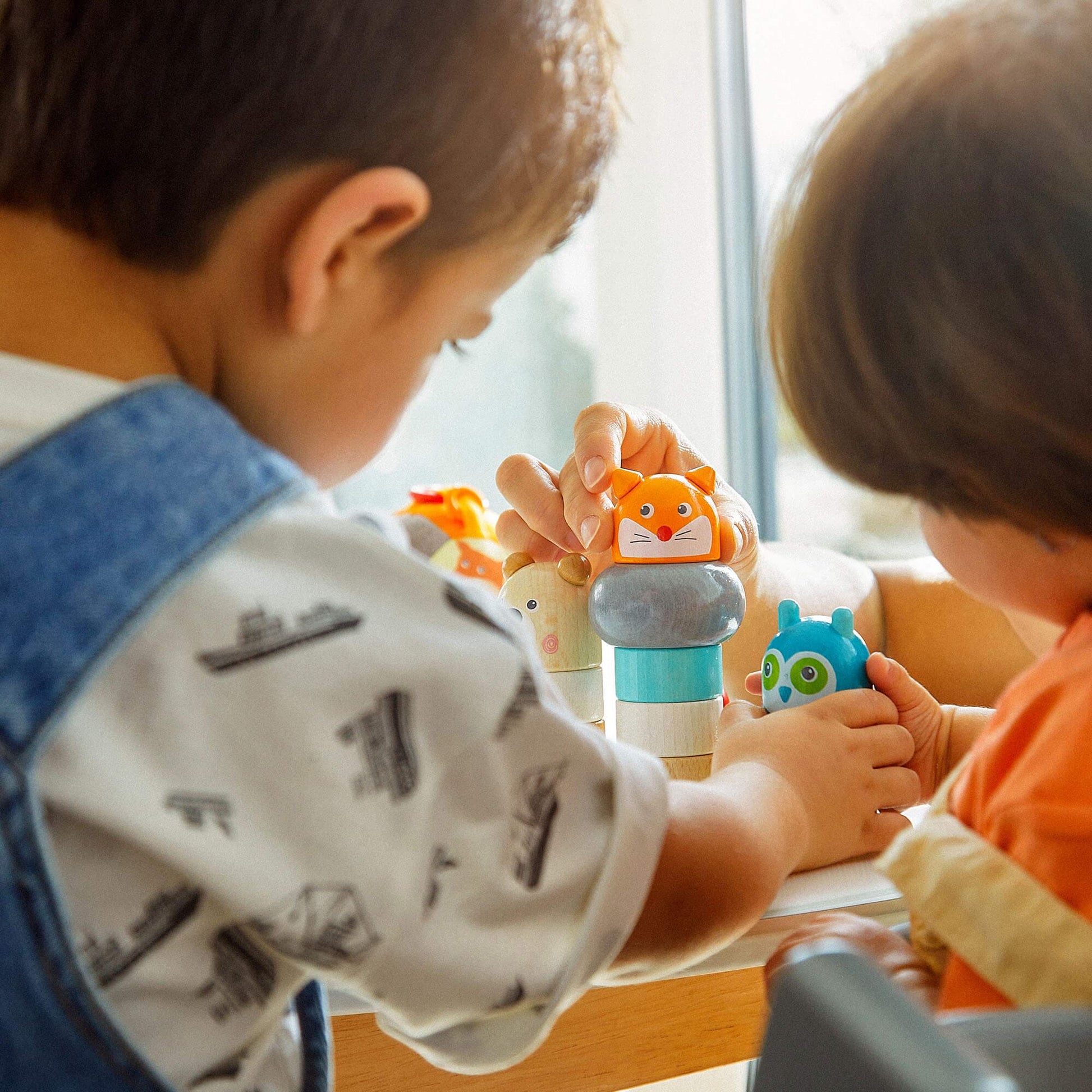 Two children playing with colorful toys at a table near a window.