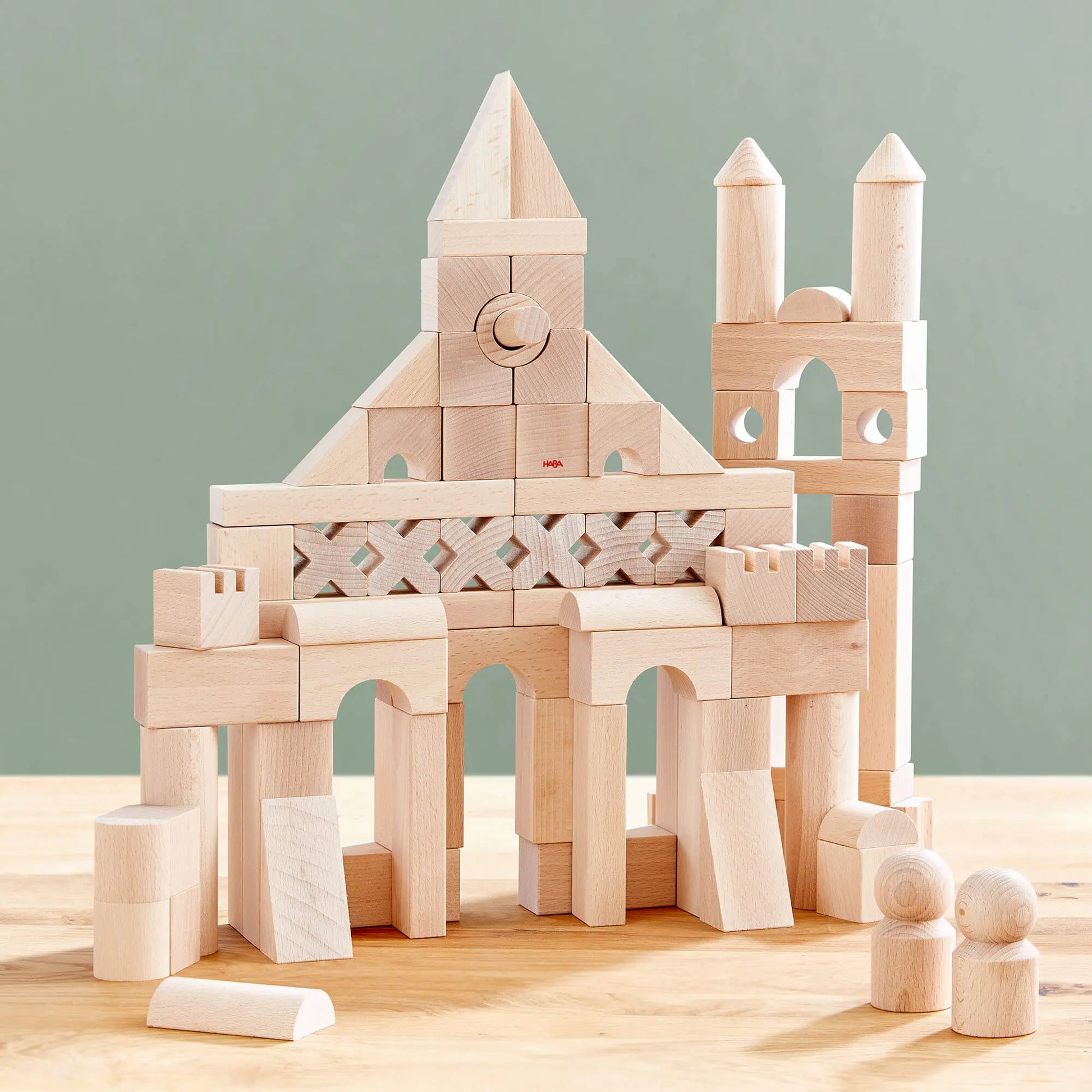 Wooden building blocks assembled into a castle structure on a wooden surface with a light green background.