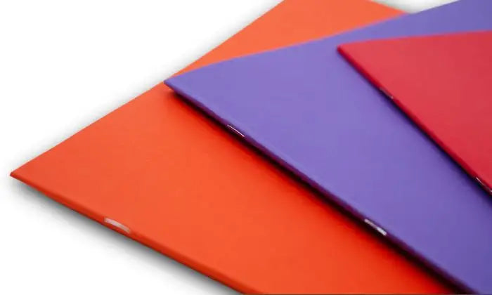 Three colorful main lesson books in red, purple, and blue showing stapled binding