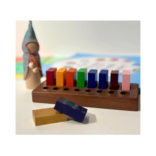 Block crayons in multiple colors in a wooden holder with peg doll gnome and blurred background