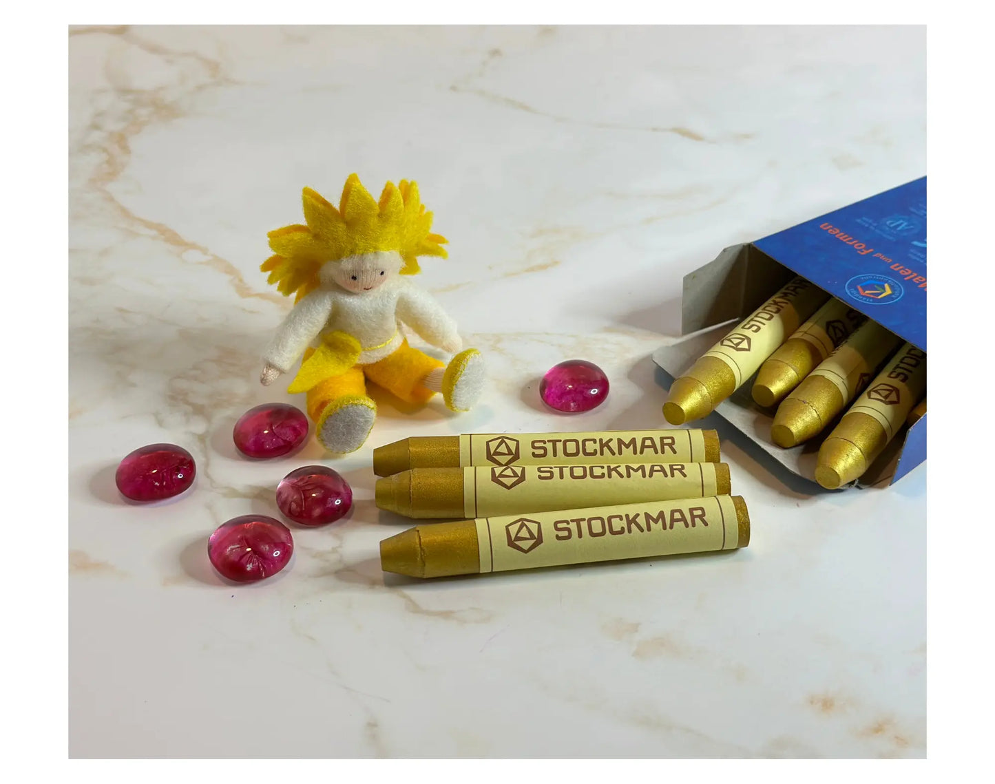 Stockmar gold stick crayons with a small figurineand pink glass beads on marble surface