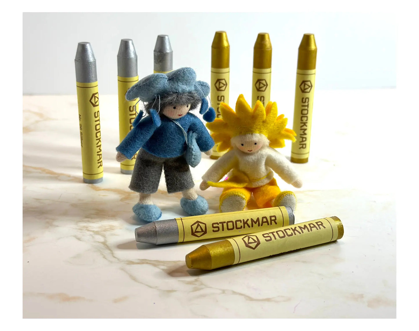 Two small dolls with colorful hair styled on top of Stockmar gold and silver stick crayons