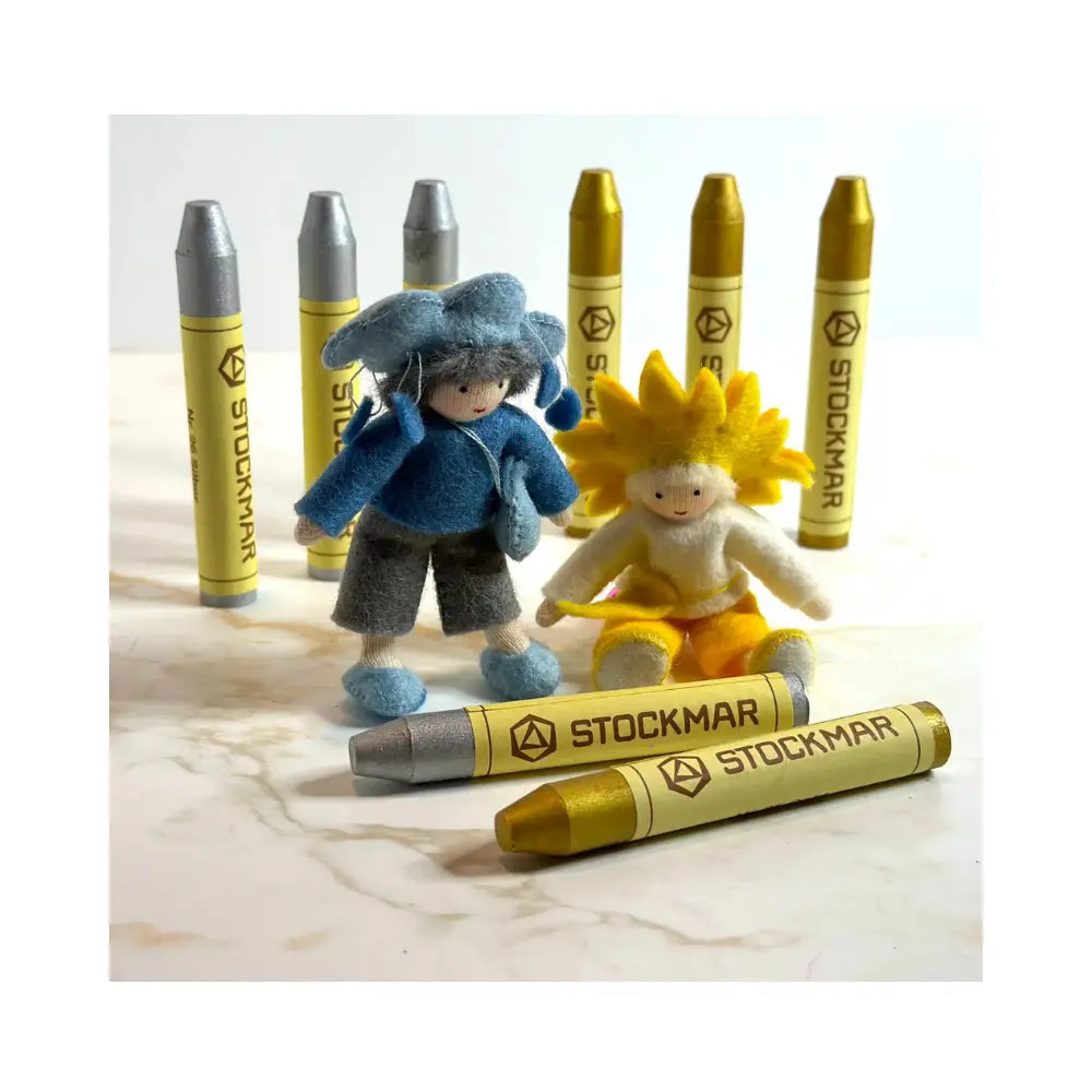 Two small figurines with Stockmar crayon-like containers on a marble surface.