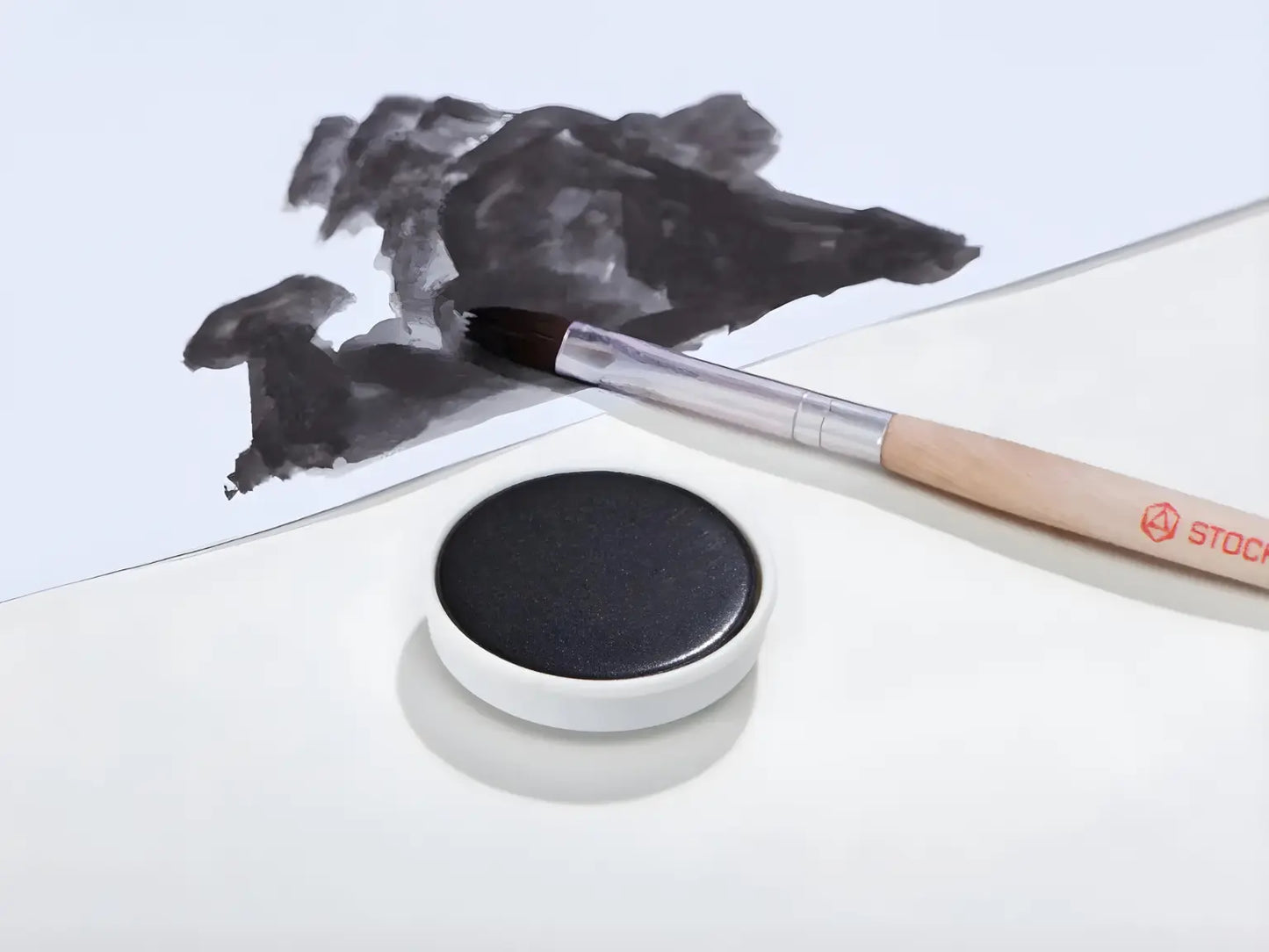 Black Stockmar opaque paint with a brush on a white background