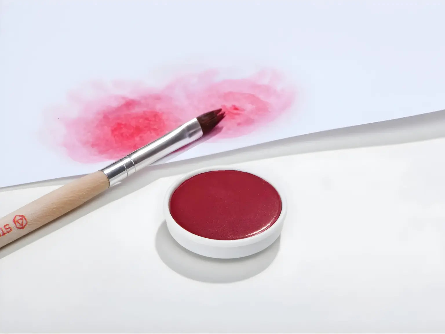 Carmine red Stockmar opaque paint with a brush on a white background