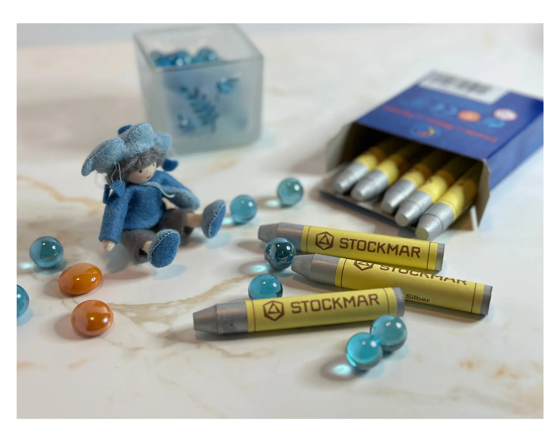 Stockmar crayons with a small figurine and colorful marbles on a light surface