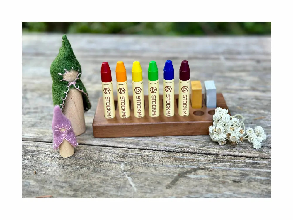 Set of colorful crayons on a wooden stand with peg dolls and flowers on a rustic wooden surface.
