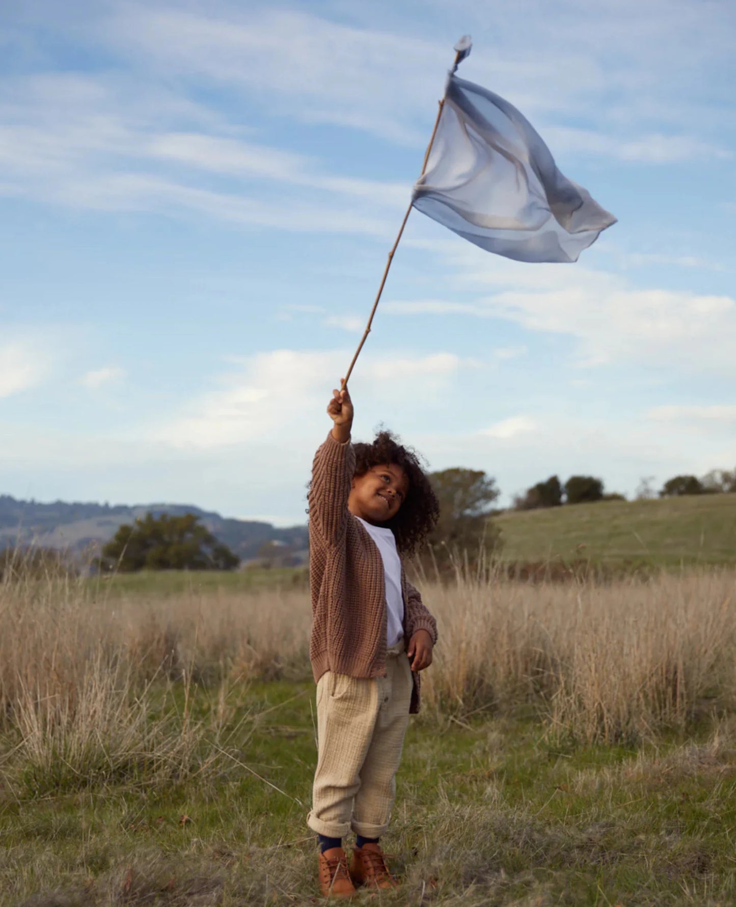 Earth playsilk in stone tied to a stick waved in air by a girl in a grassy field