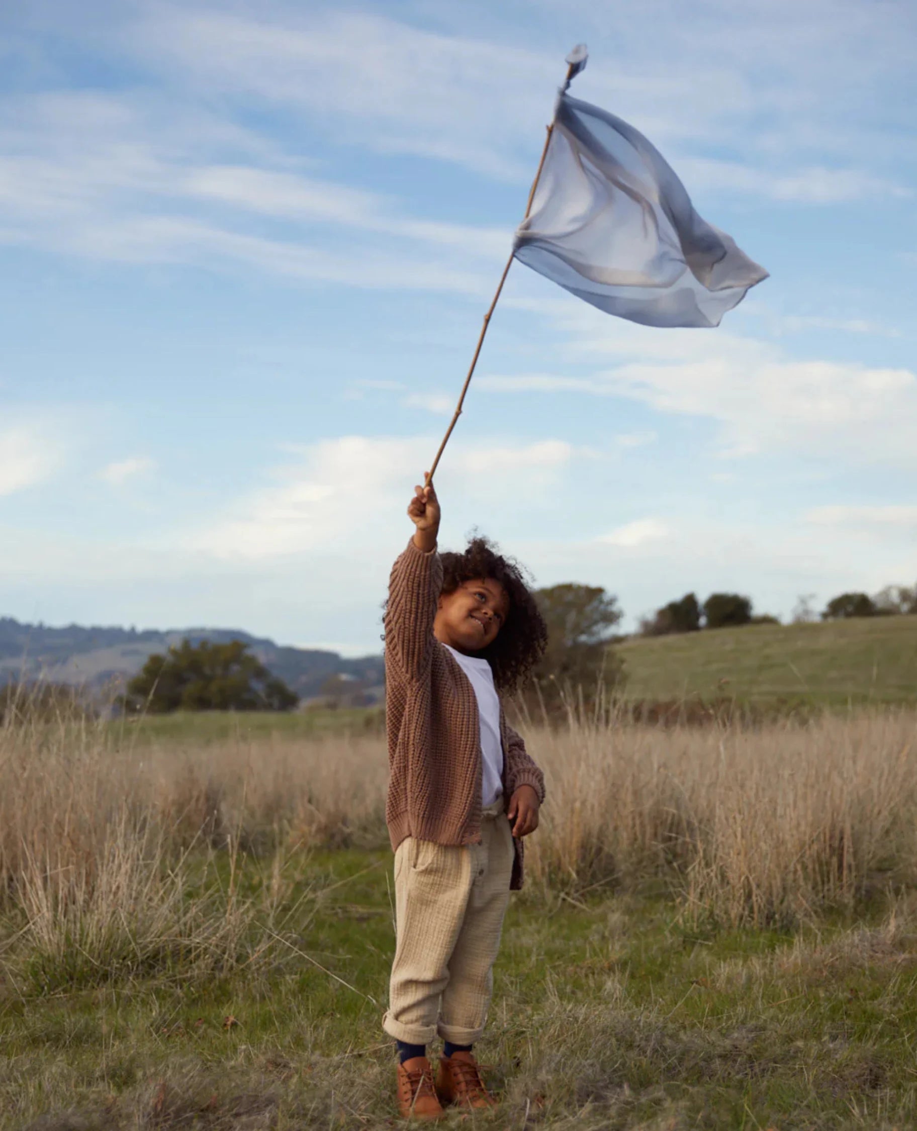 Earth playsilk in stone tied to a stick waved in air by a girl in a grassy field