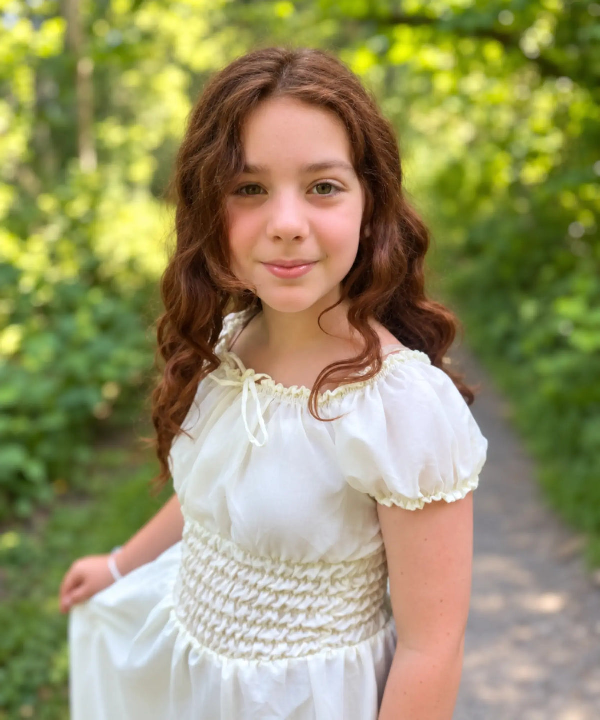 Child wearing the white smocked chemise underdress on a woodland path, showing the gathered neckline, puff sleeves, and smocked waist.