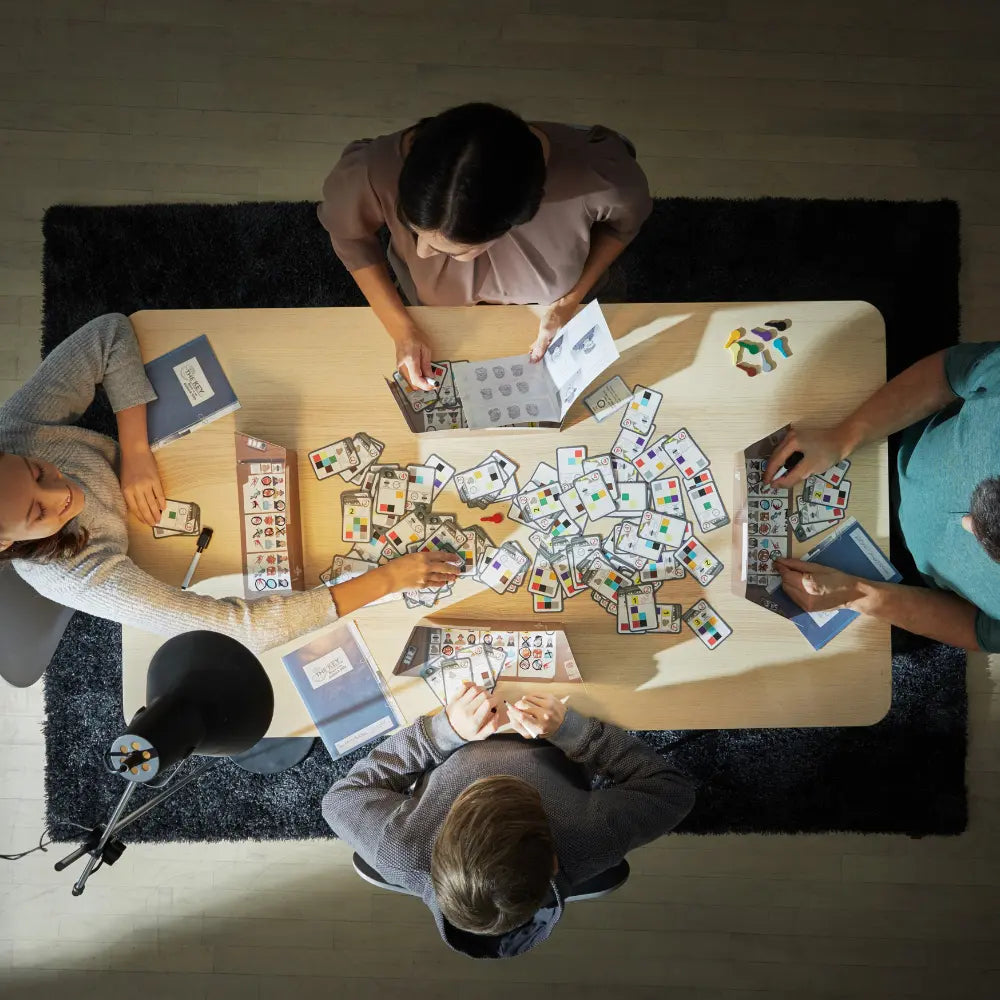 Four people playing a card game around a table with various cards spread out.