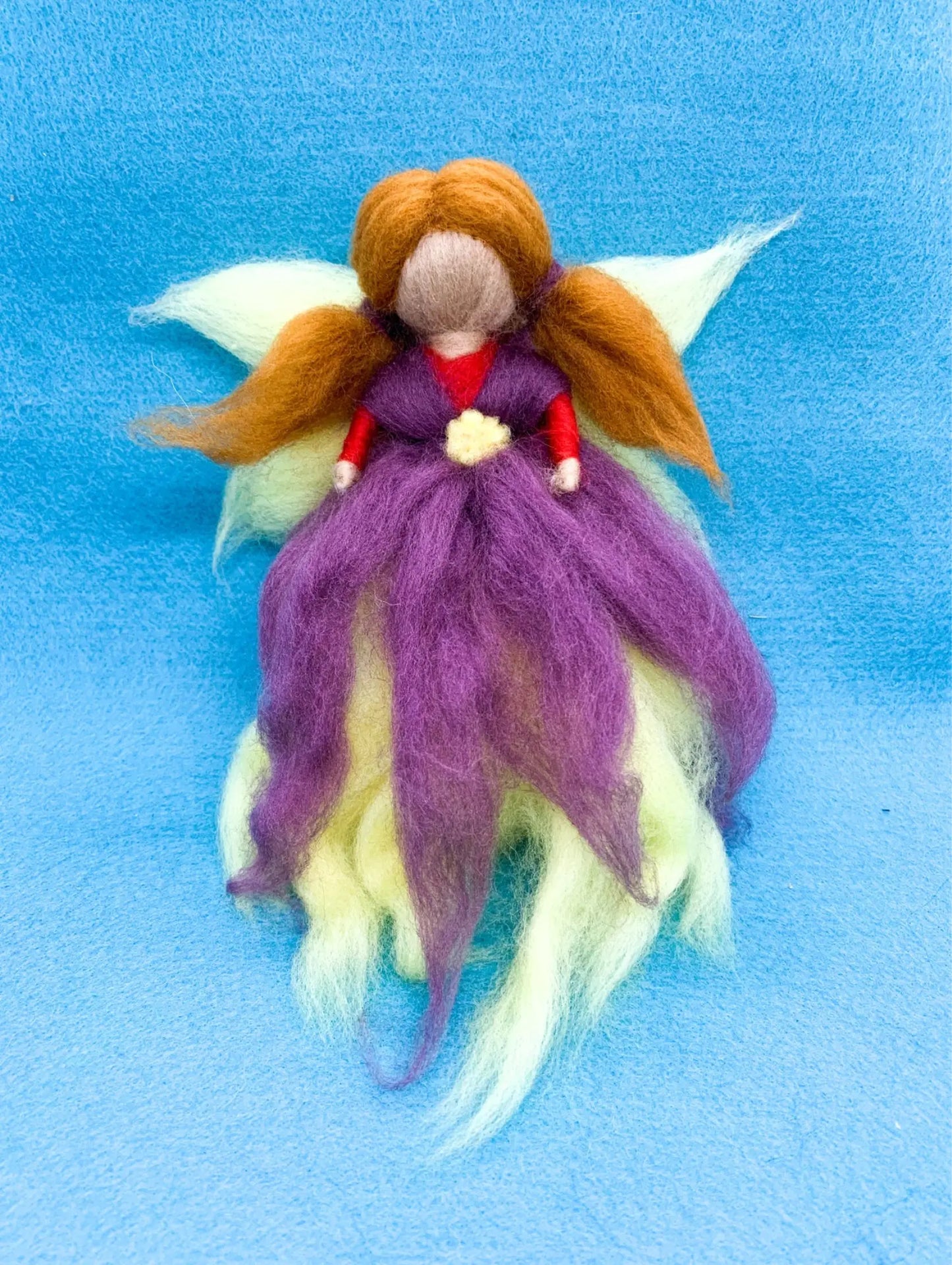 Felted fairy doll with purple dress and red shoes on a blue background