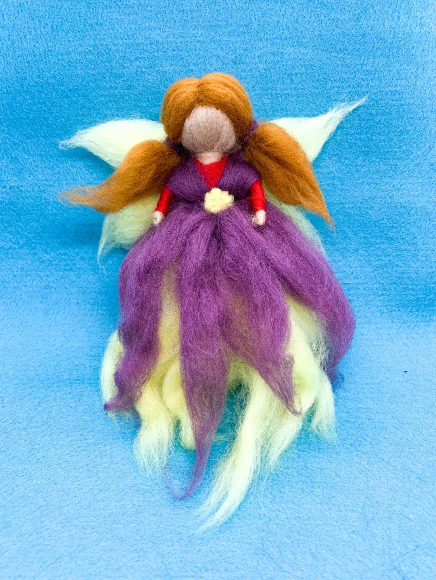 Felted fairy doll with purple dress and red shoes on a blue background