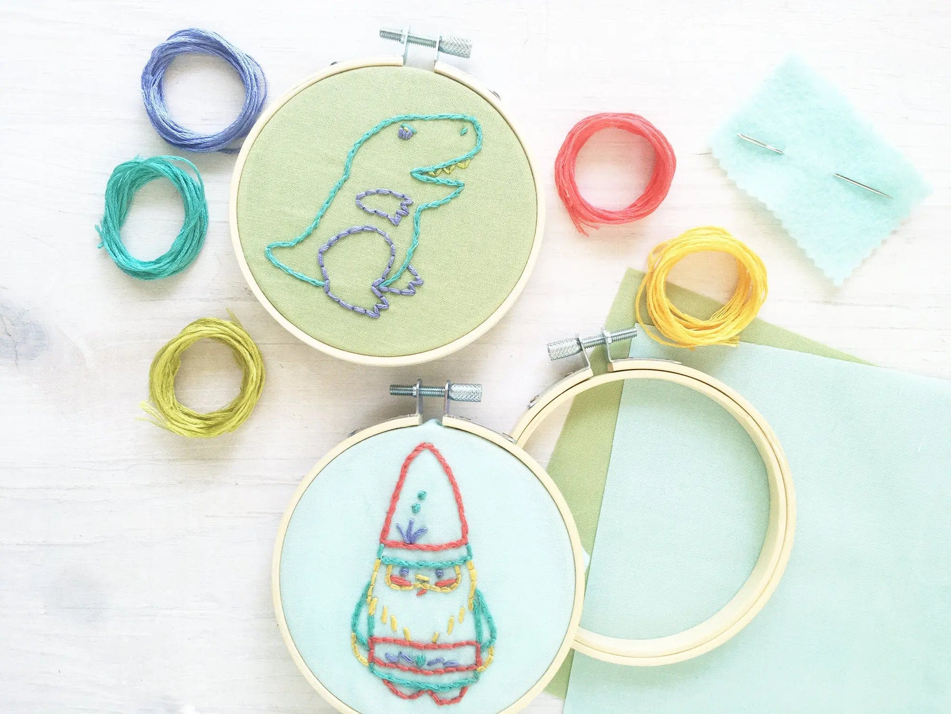 Embroidery hoops with dinosaur and rocket designs on a light background