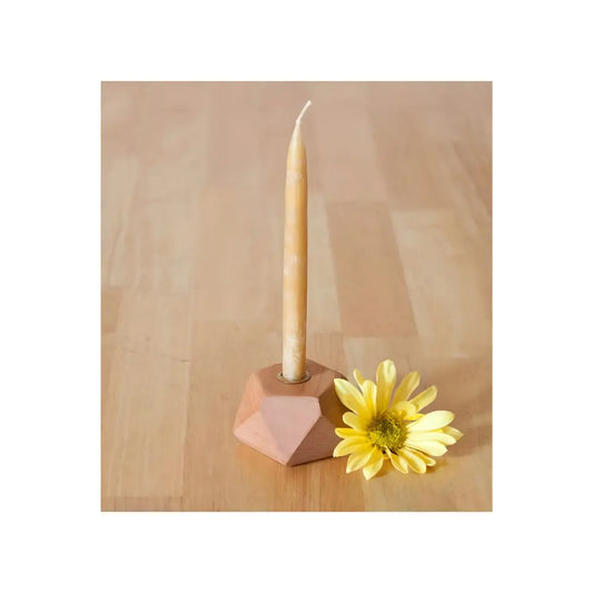 Candle in a geometric holder with a yellow flower on a wooden surface