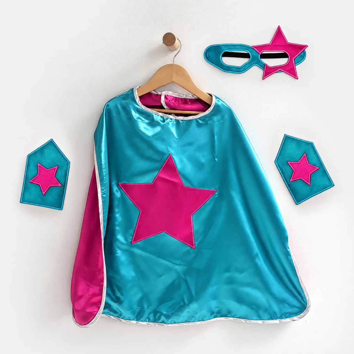 Teal superhero cape set with magenta star emblem, matching eye mask, and wrist cuffs.