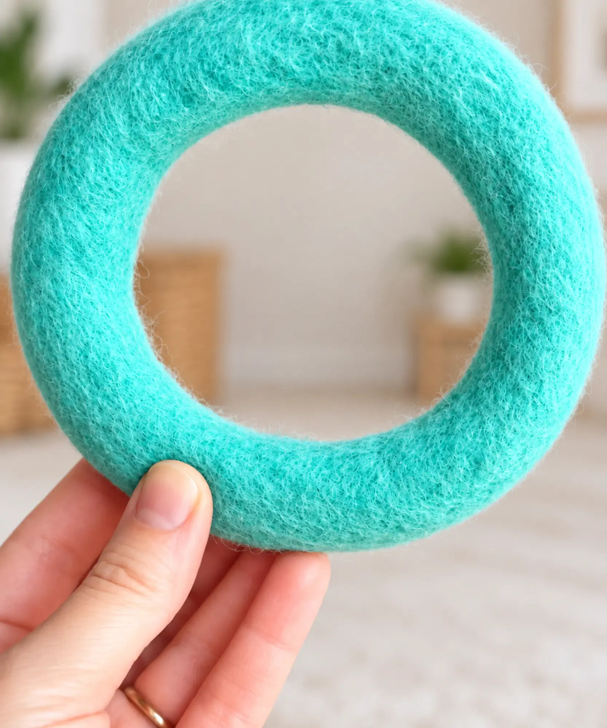 A hand holding a teal wool felt ring about 3 inches across, showing its size.