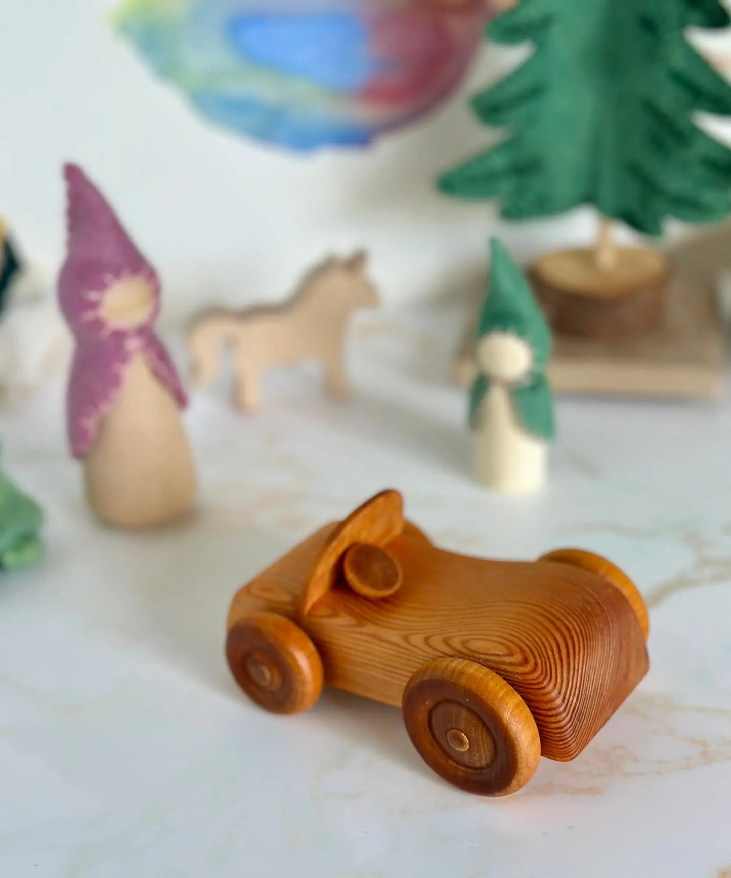 Wooden toy car on a surface with other small figurines in the background