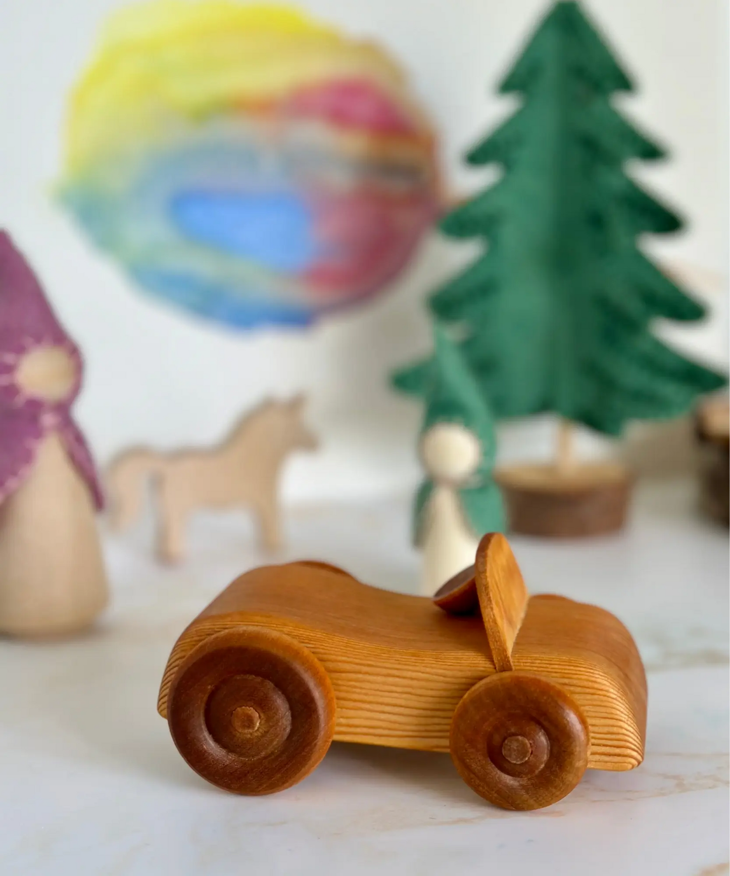 Wooden Telleby toy car on a surface with blurred small play scene in the background