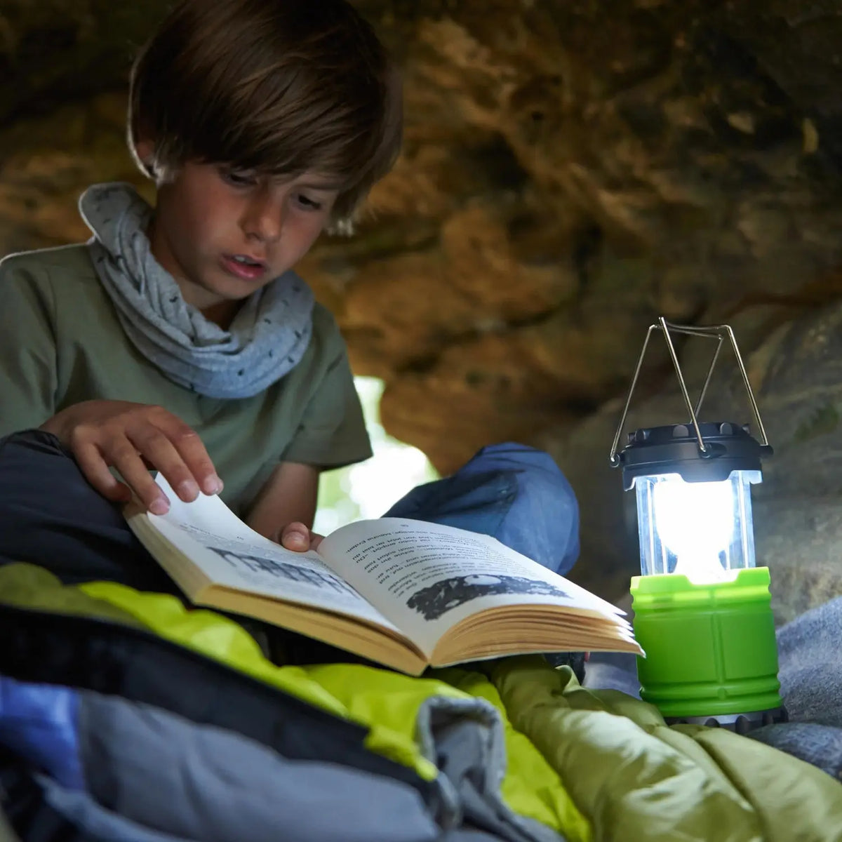 Child reading beside the illuminated Terra Kids Camping Lantern during an outdoor adventure