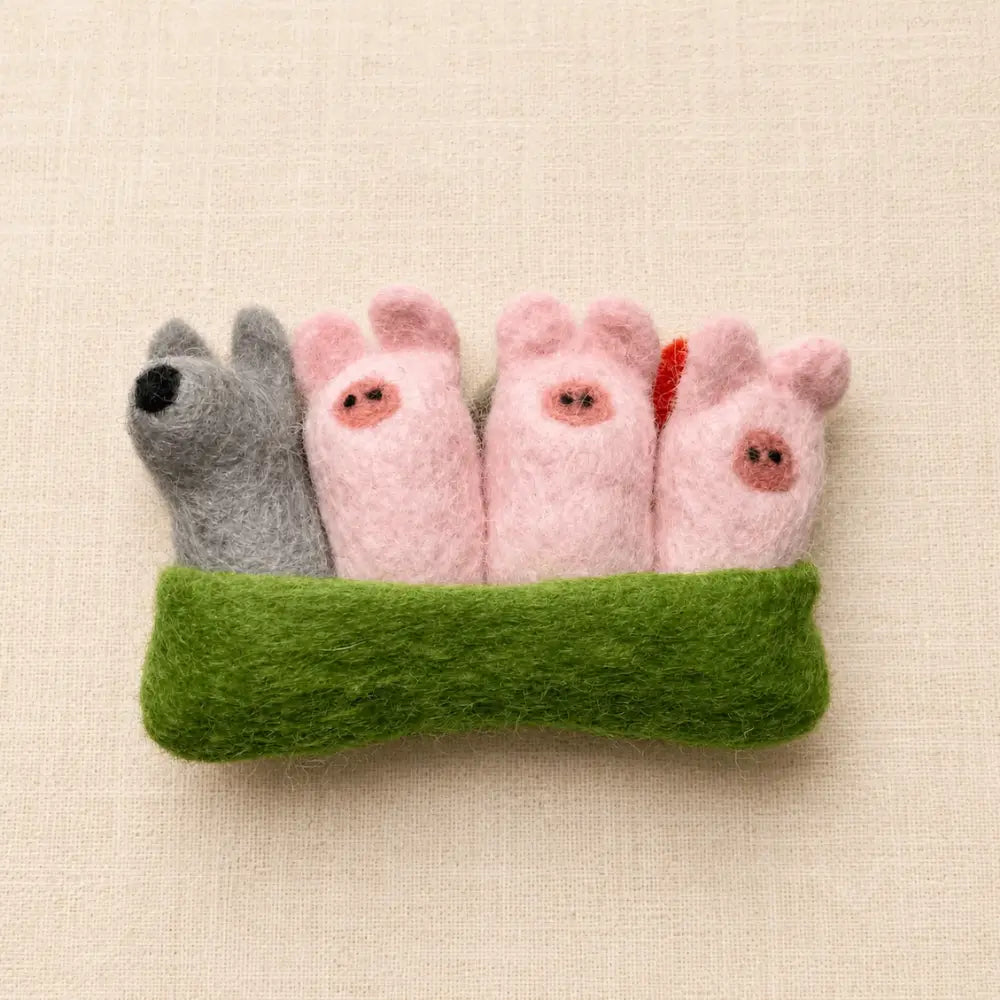 Three Little Pigs felt storytelling set with three pigs, wolf, felt houses, and green pouch on a cream linen background.