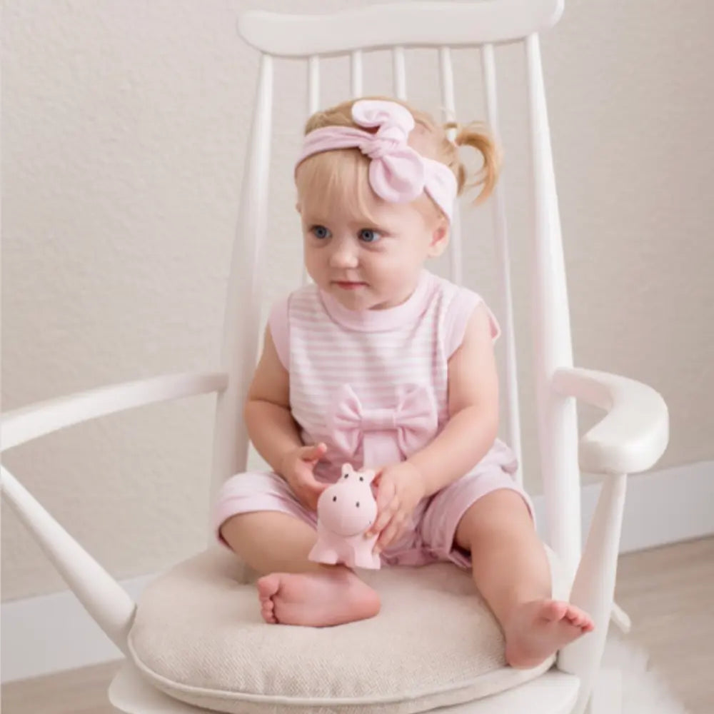 Toddler holding natural rubber hippo teether while seated during play
