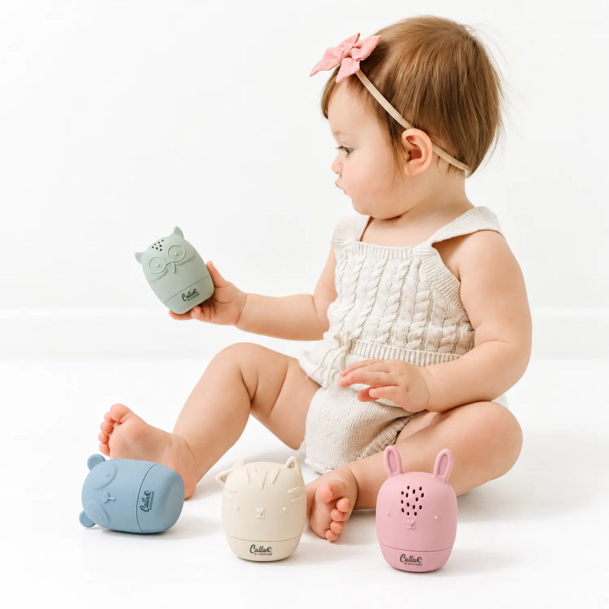 Toddler holding a sage green silicone owl bath toy with other animal water toys nearby