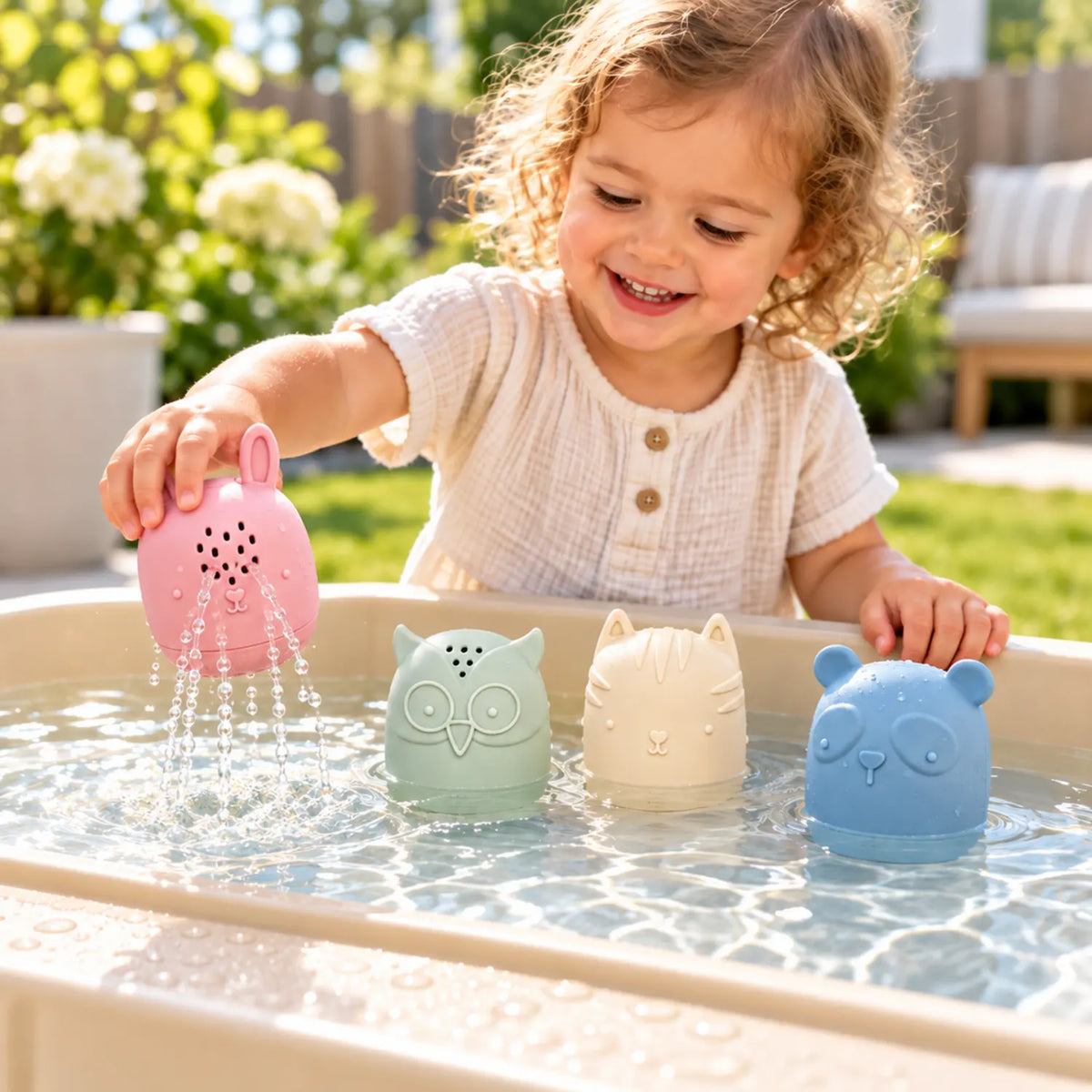 Toddler playing with silicone animal water toys at a sunny outdoor water table