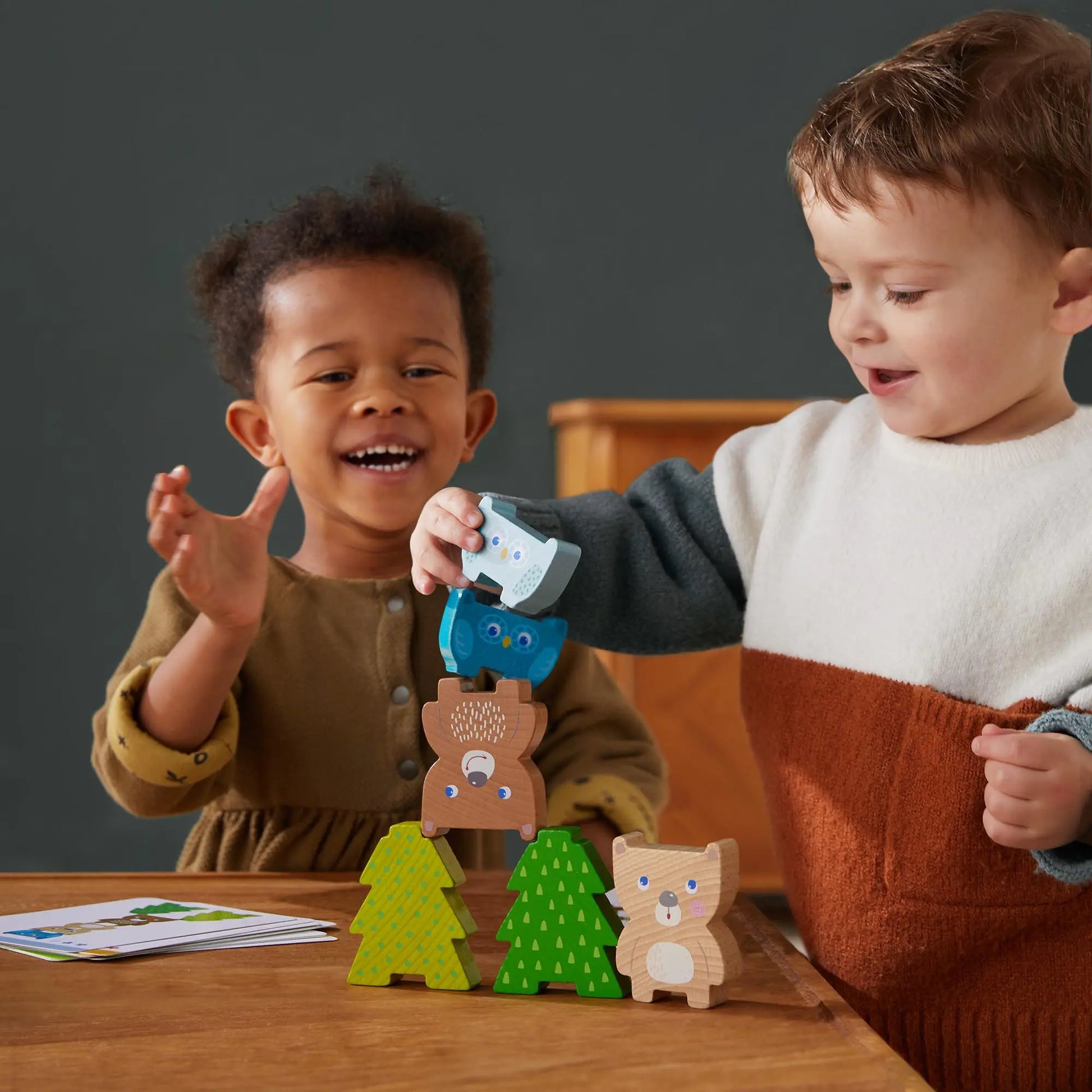 Two children playing with wooden animal toys on a table.