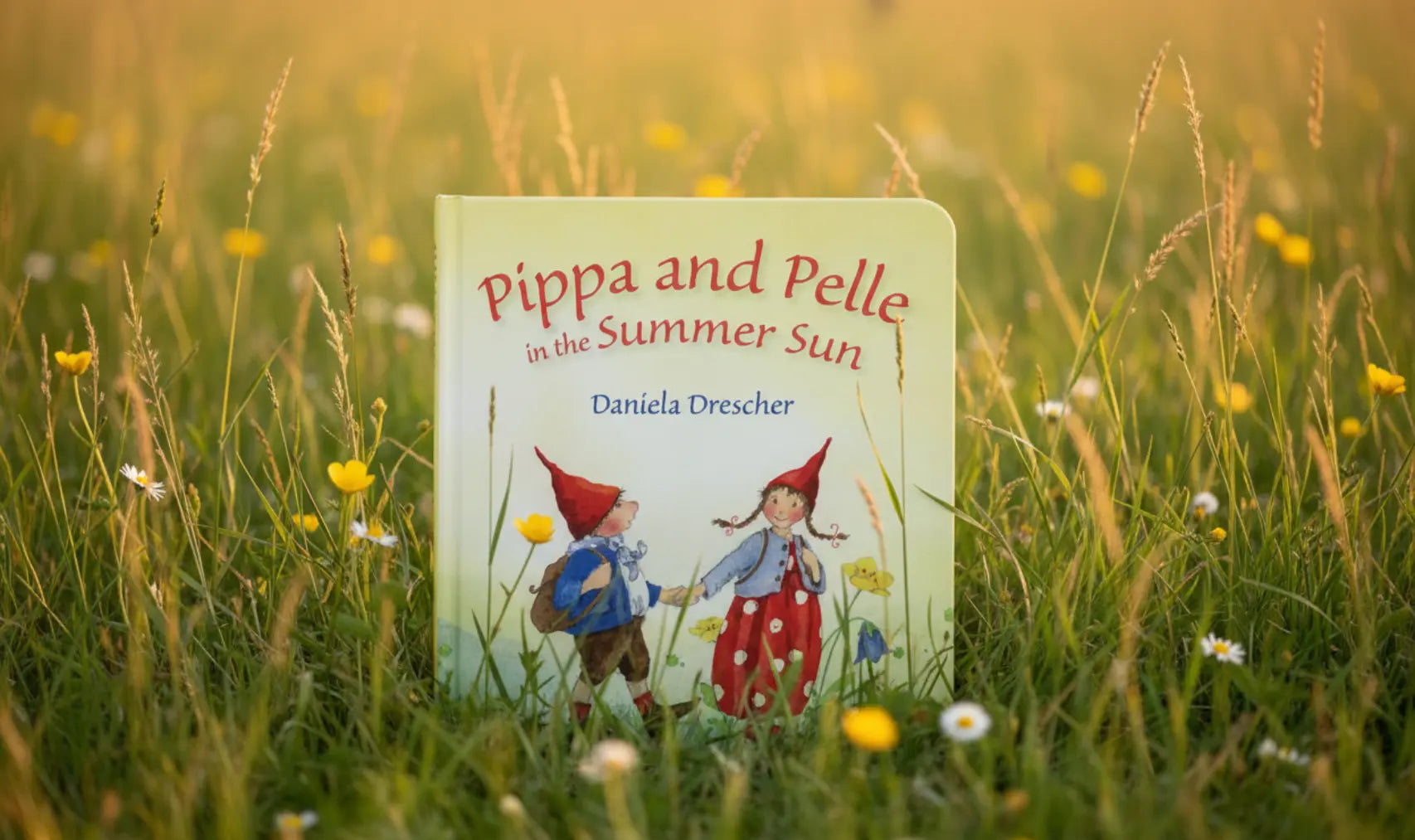 Book titled 'Pippa and Pelle in the Summer Sun' by Daniela Drescher in a grassy field with flowers.