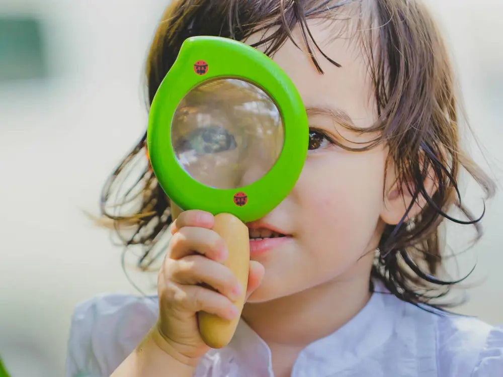 Child holding a green magnifying glass up to their face