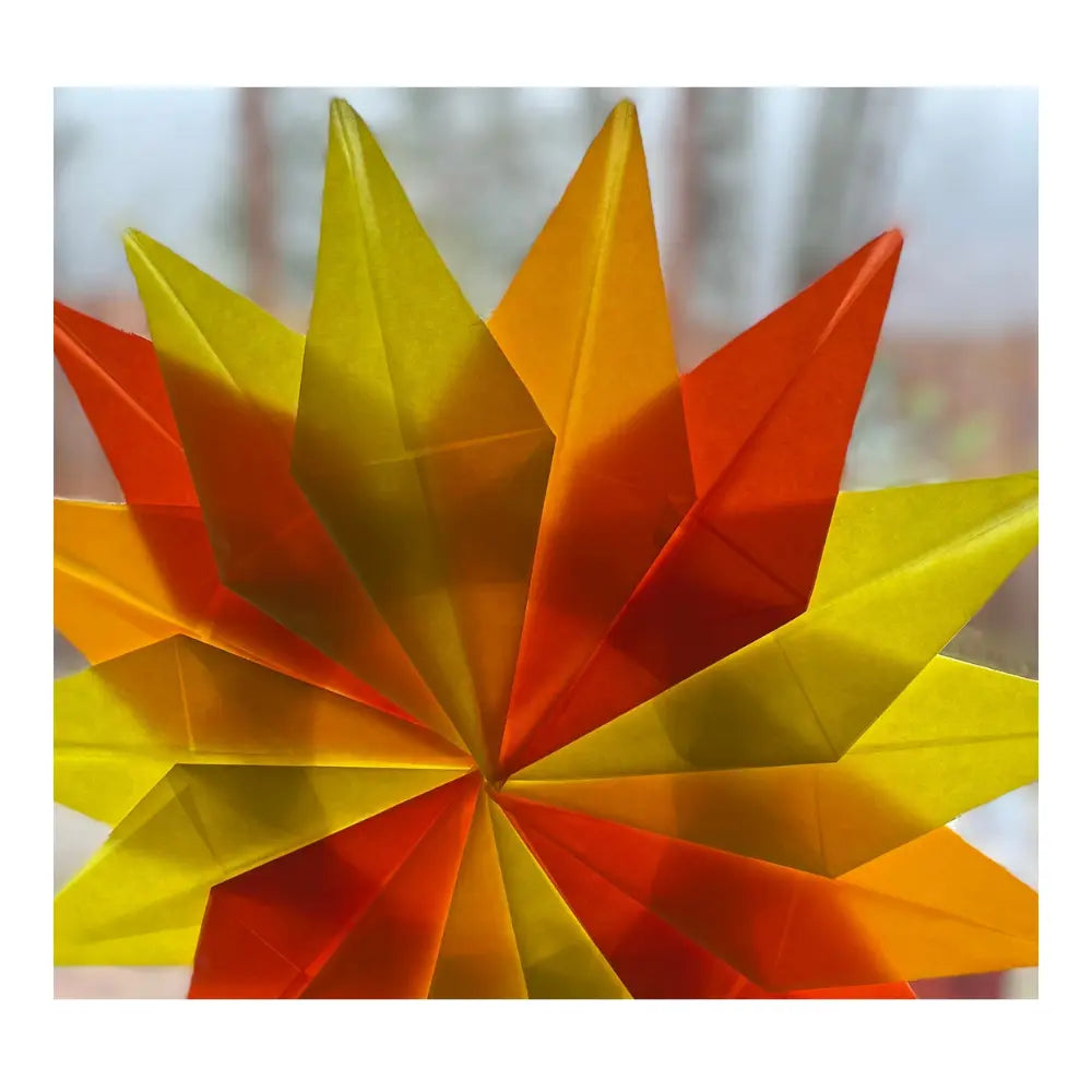 orange, yellow, and dark orange waldorf window star made from kite paper on a window