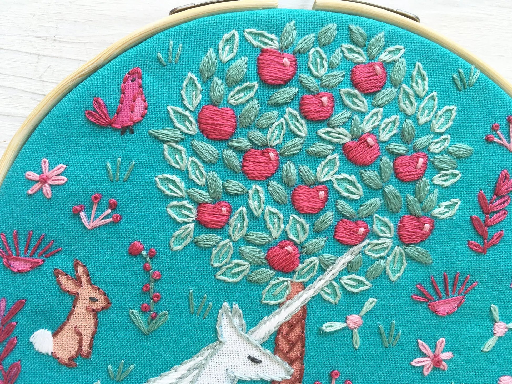 Embroidery hoop with close up detail of a tree, rabbit, and unicorn on a teal fabric