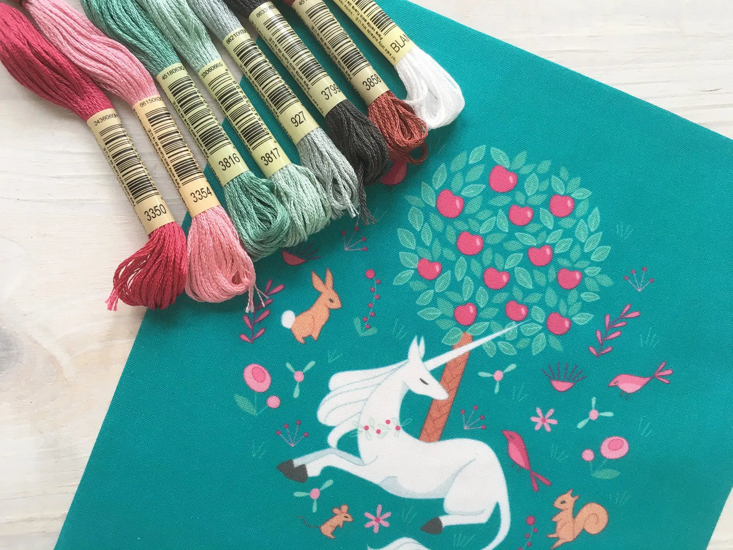 Embroidery threads on a teal embroidery fabric with unicorn and tree design